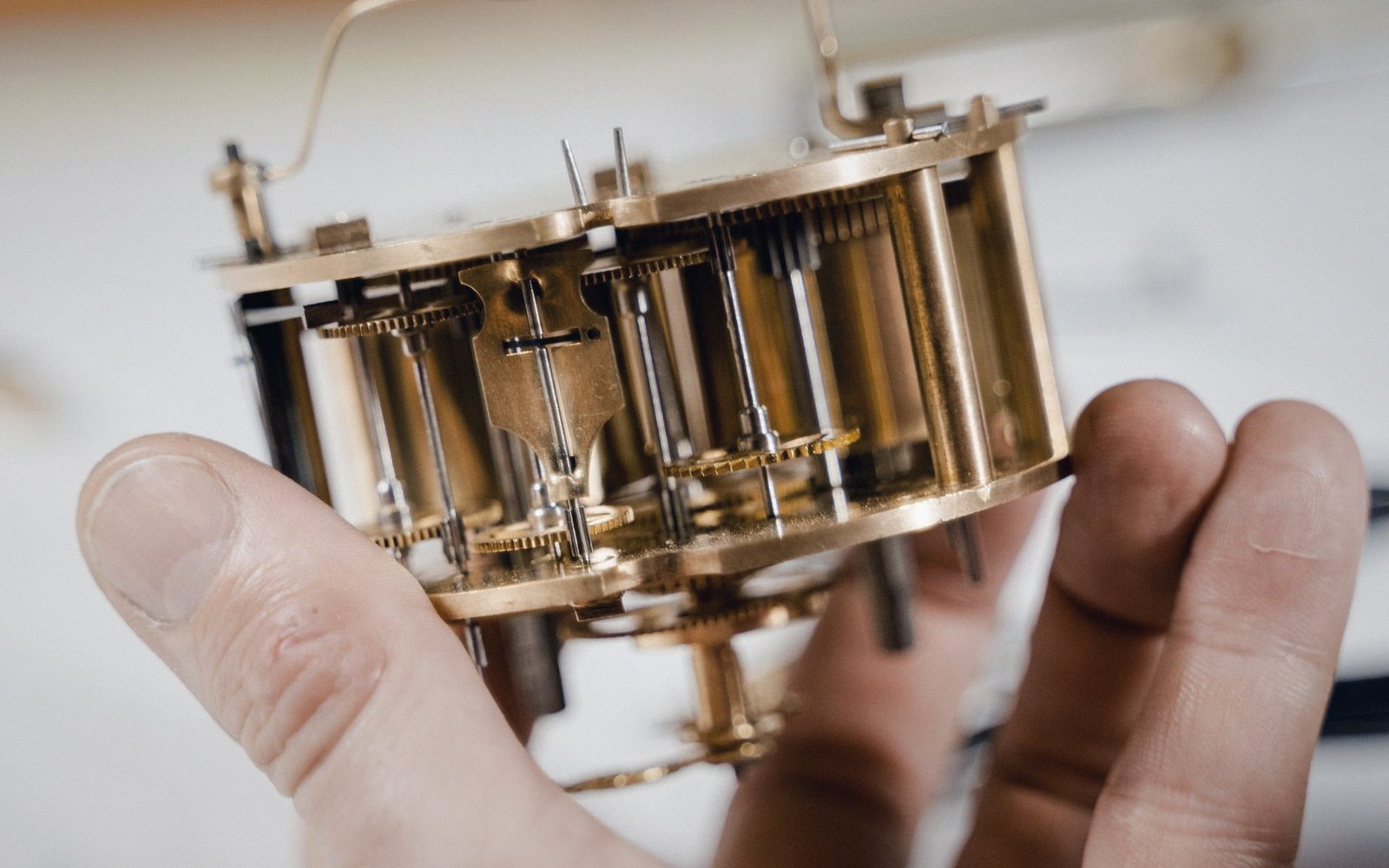 A hand holds a brass clock movement showing its gears and mechanical components