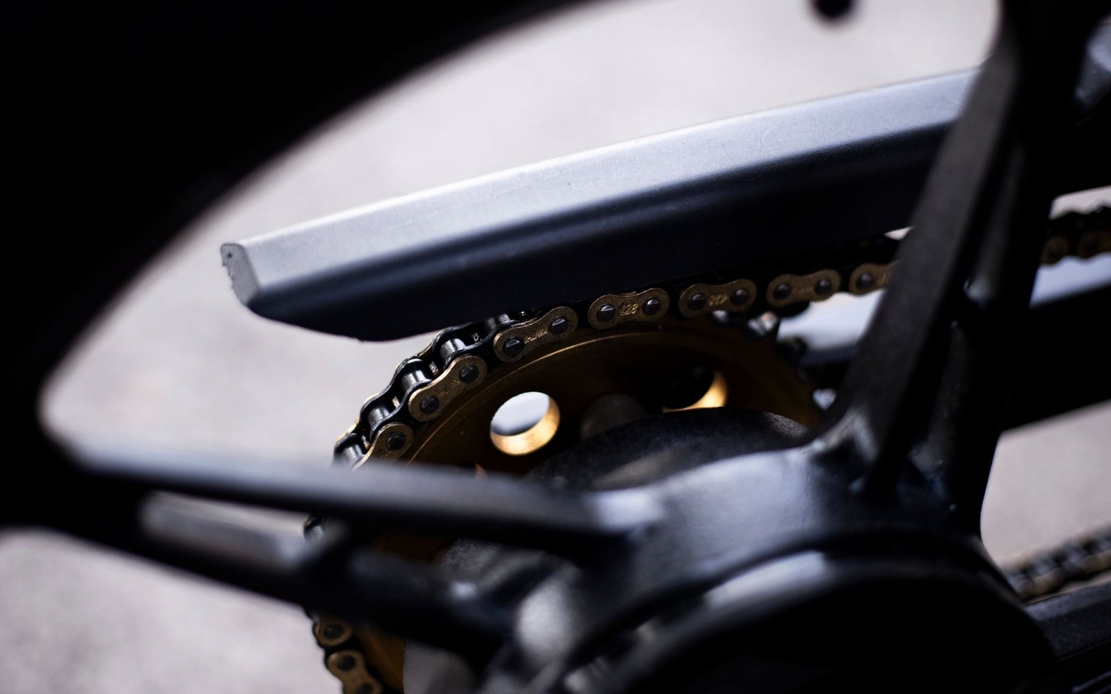 Close-up of a bicycle's gold chainring and chain beneath the frame and crank arm