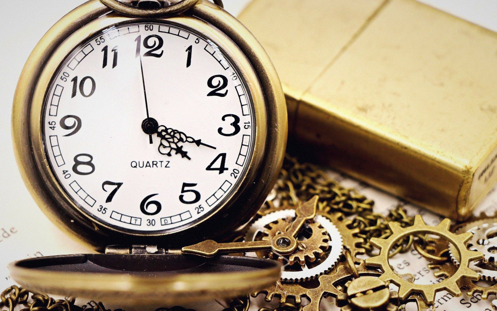 An open brass pocket watch resting among metal gears beside a brass lighter