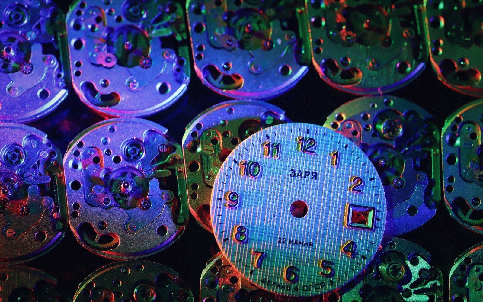 Rows of watch movement parts surround a Zarya clock face under colorful neon lighting