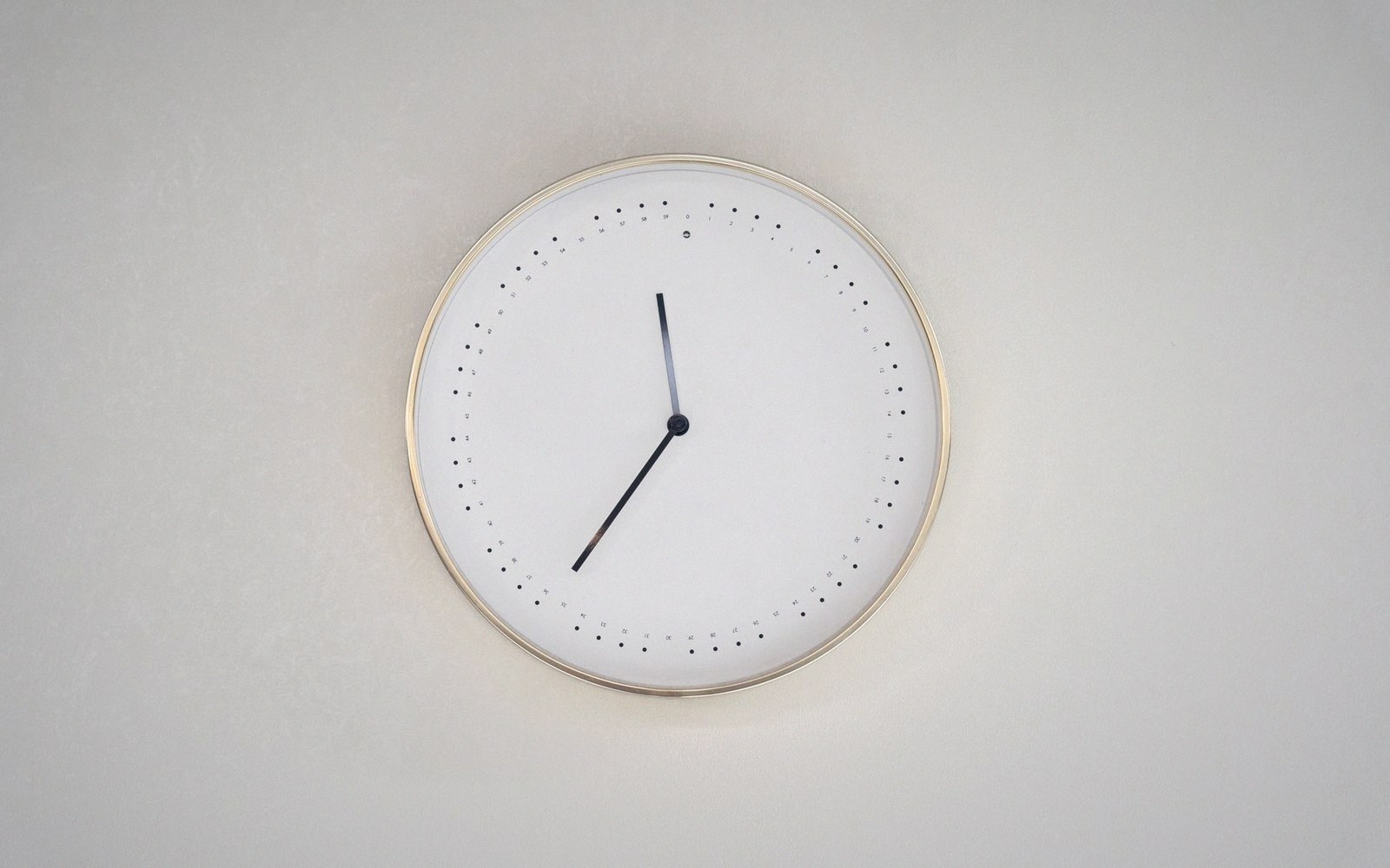 A minimalist round wall clock with dot markers and a gold-toned rim